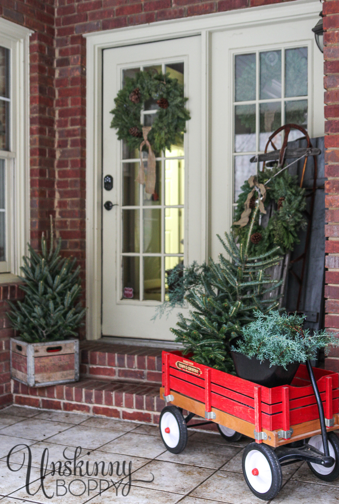 Evergreen trees in a red wagon and sled on a Christmas porch