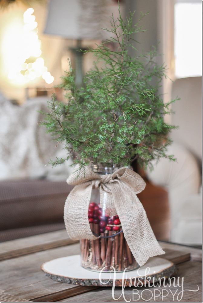 Simple holiday table centerpiece- evergreen in a glass vase filled with cinnamon sticks and cranberries tied with a burlap bow.