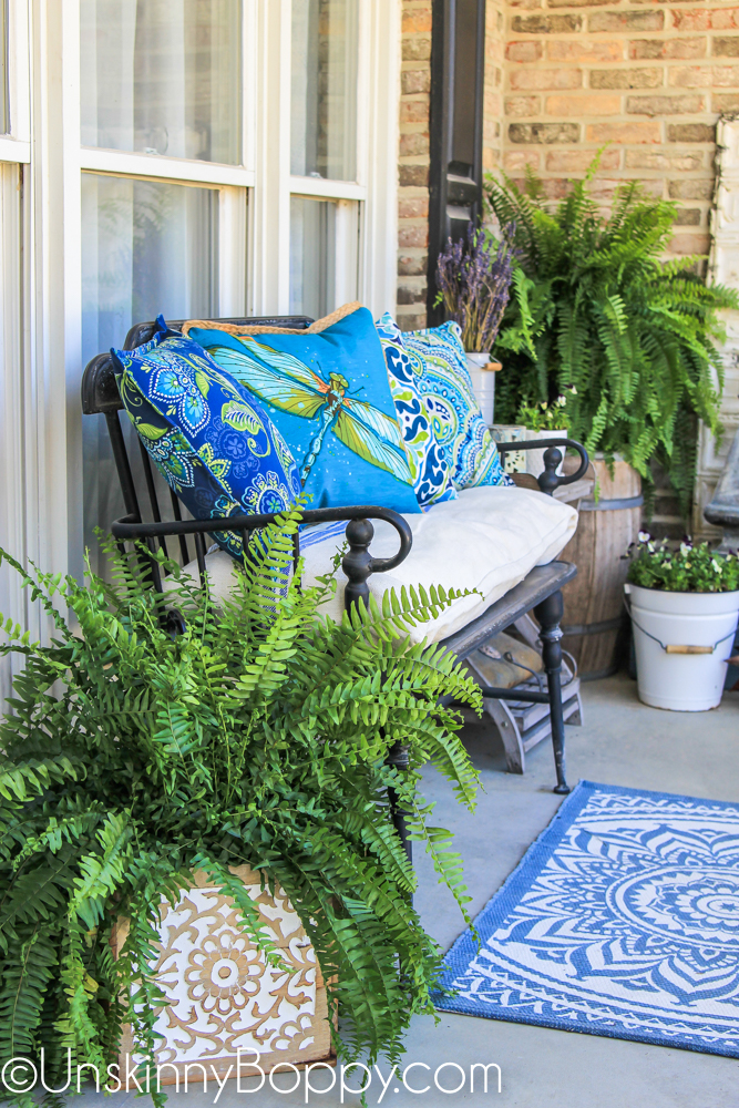 Black wrought iron bench with blue dragonfly pillows on porch