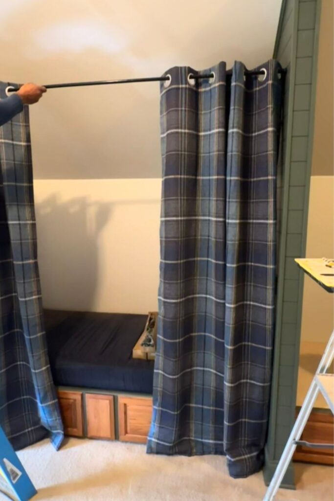 navy blue plaid tartan grommet curtains being hung on black iron rods at attic bunk room nook openings with curtain bottoms just touching the carpet