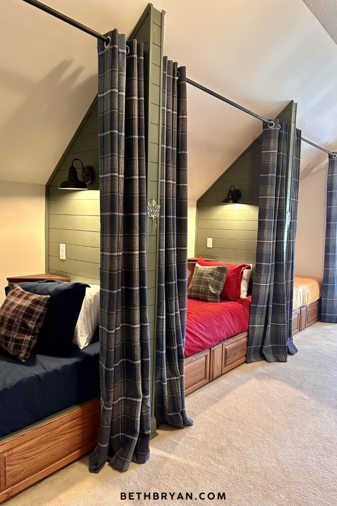 finished attic bunk room with five built-in sleeping nooks painted Sherwin-Williams Pewter Green SW 6208 navy plaid curtains on black iron rods jewel tone bedding and retractable ceiling fan light