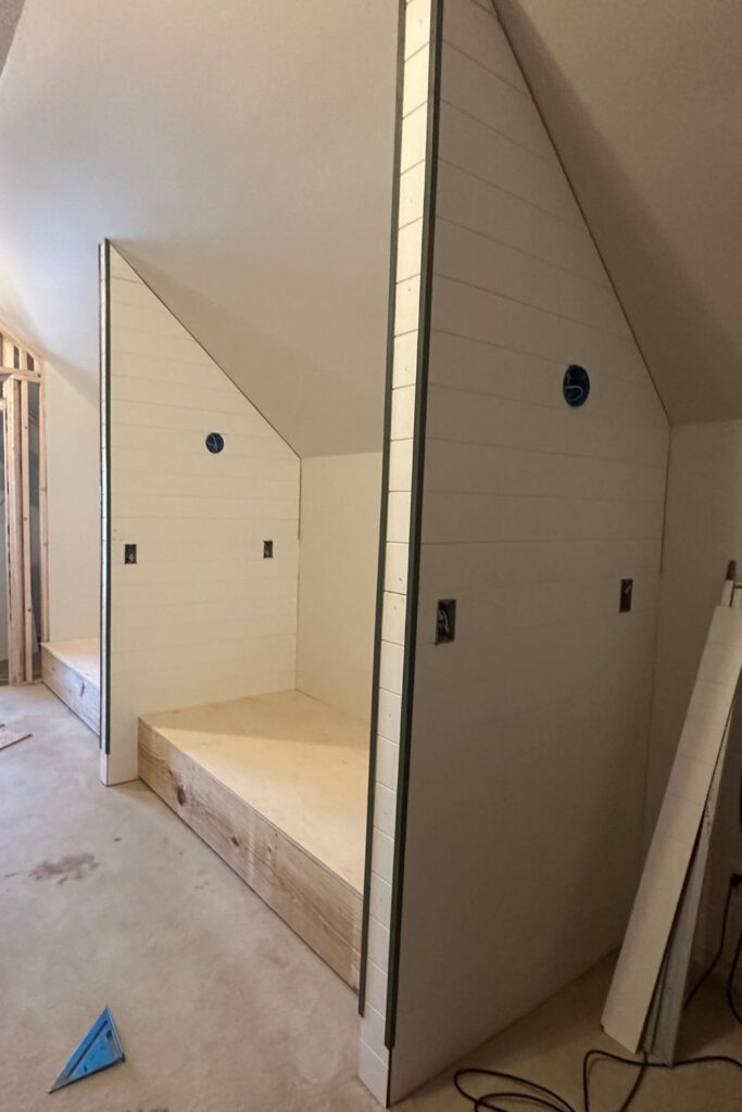shiplap wall panels being installed in attic bunk nooks with electrical junction boxes roughed in for hardwired sconces and outlets before painting