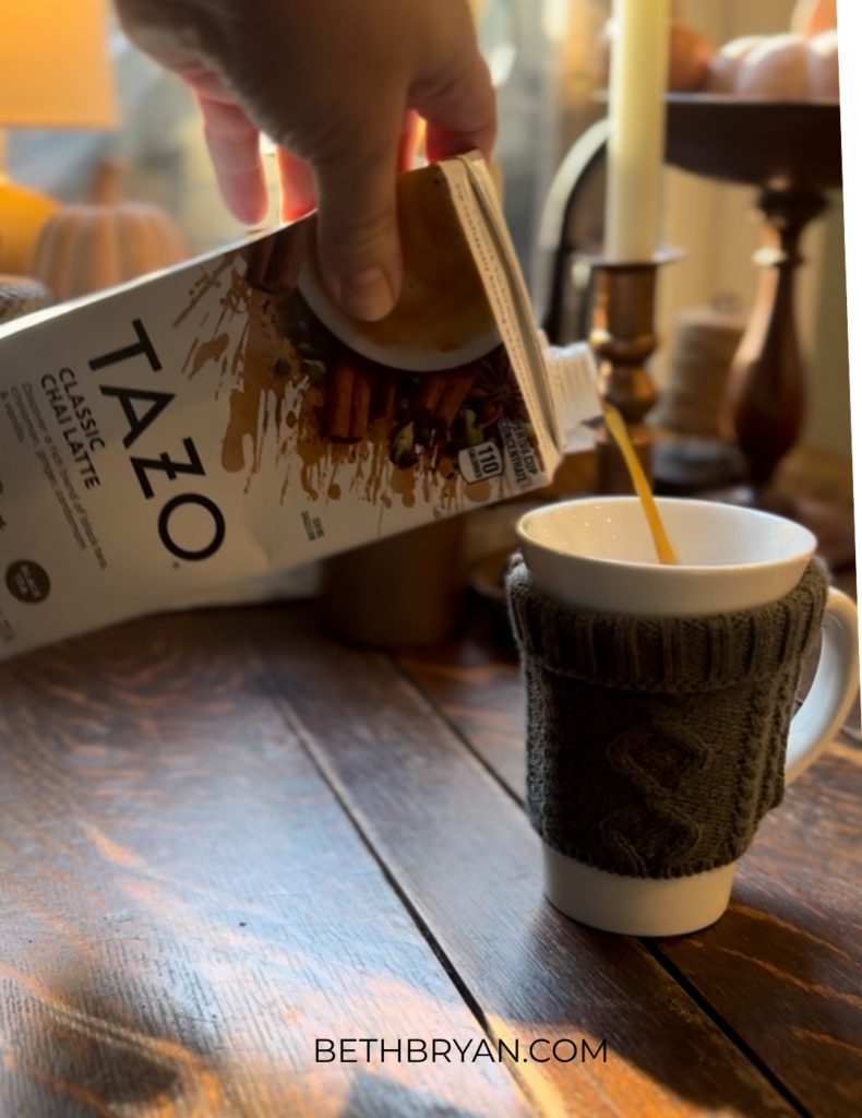 how to make starbucks copycat chai latte at home - wooden table with Tazo chai tea concentrate pouring into mug with sweater